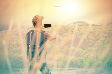 Freedom traveler man standing and take a photo with smart phone enjoying a beautiful nature. Image with vintage filter effect.の写真素材