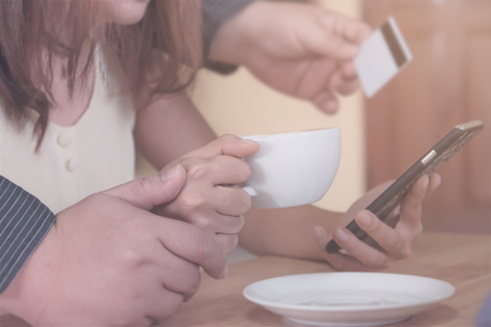 close up of hand holding cup of coffee, man holding credit card and woman using smart phone as online shopping concept. vintage filter effect.の写真素材