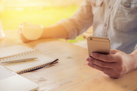 business man using smart phone and write on notebook and laptop on wooden desk outdoor office with morning light. Vintage filter effect.の写真素材