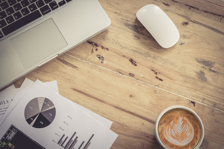 Top view with graph chart and laptop and mosue and cup of coffee on wooden desk in office with copy space. vintage filter effect.の写真素材