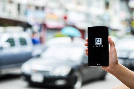 CHIANG MAI,THAILAND - JULY 17, 2016 : A man hand holding Uber app showing on LG G4 on road and red car, Uber is smartphone app-based transportation network.のeditorial素材