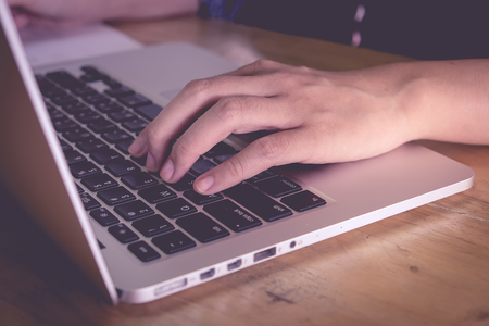 Woman's hands using laptop with blank screen on desk in coffee shop. Vintage filter effect.のeditorial素材