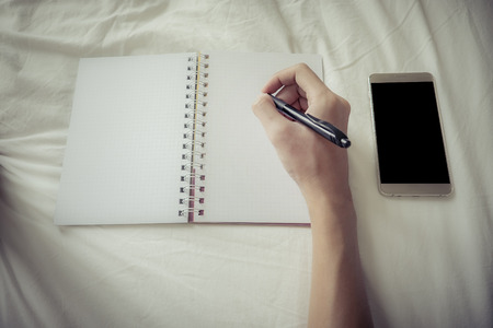 Business man laydown on bed and hand holding pen for working in bedroom with smartphone blank screen. vintage.の写真素材