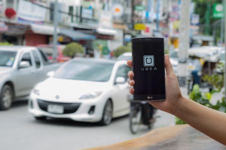 CHIANG MAI,THAILAND - JULY 17, 2016 : A man hand holding Uber app showing on LG G4 on road and red car, Uber is smartphone app-based transportation network.のeditorial素材