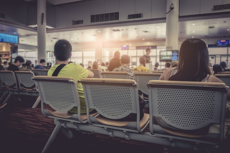 people at international airport, sitting on chair while waiting for flight. passenger at terminal, indoors.のeditorial素材