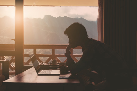 Business man using laptop with cup of coffee on wooden table at workplace and mountain view form window.の写真素材