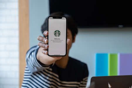 Chiang Mai, Thailand : Mar 19 2021 : Asian man showing Starbucks logo on iPhone screen in Starbucks...