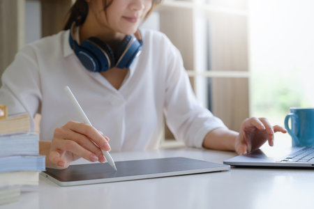 Fashion designer using tablet and sketches while working at table in studio.
