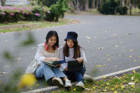 Two students are sitting in university during reading a book and communication. Study, education,...