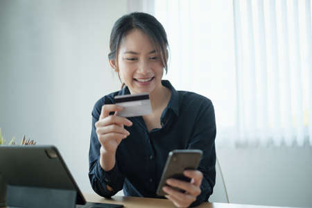 Woman in casual shirt paying with credit card online while making orders via application on cell...
