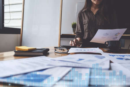 Close up Business woman hand holding pen and calculating with paperwork and virtual stock chart.の写真素材