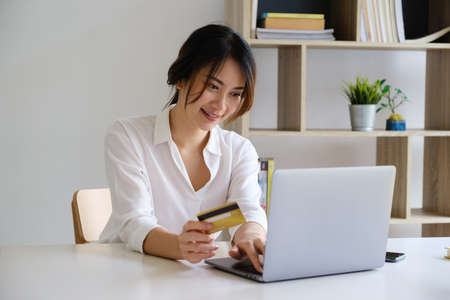 Woman enjoy with online shopping application and looking at laptop for fill credit card number to...