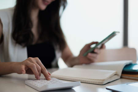 Business woman hand holding pen and cell phone with bank savings account application, account or...