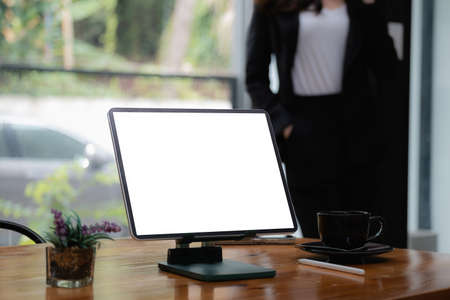 Mockup digital tablet on wooden desk with blank screen. Business people working at background.