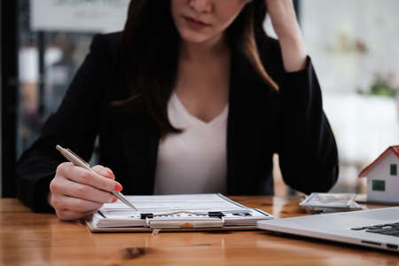 A stressed woman signs a contract to cancel her rent apartment and pay an outstanding payment.の写真素材