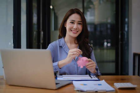 Young woman smiling putting a coin inside piggy bank as savings for investment. wealth and financial conceptの写真素材