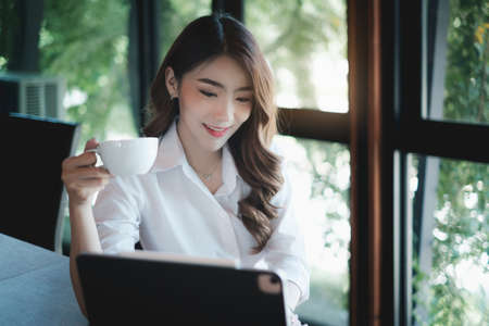 Image of beautiful business woman holds a cup of coffee and checks her email before going to workの写真素材