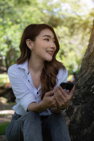 Portrait of Asian beautiful woman using smartphone at outdoor park.の写真素材
