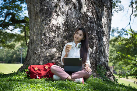 Student sitting in university park during break and research by tablet. Study, education, university, college, graduate concept.の写真素材