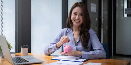 Young woman smiling putting a coin inside piggy bank as savings for investment. wealth and financial concept.の写真素材