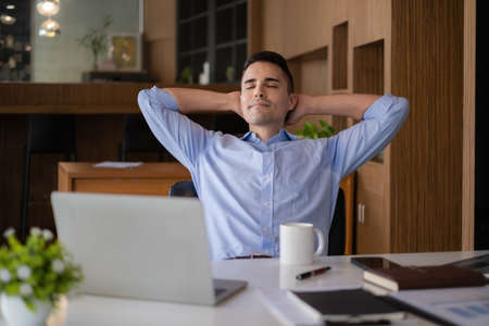 American businessman relaxing in chair after hard work at offlice. Business man with laptop on deskの写真素材