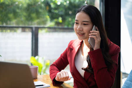 Asian employee talking with speaker phone and video call by smartphone in home office. Business financial concept.の写真素材
