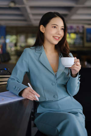 Image of beautiful business woman holds a cup of coffee and checks her email before going to work.の写真素材