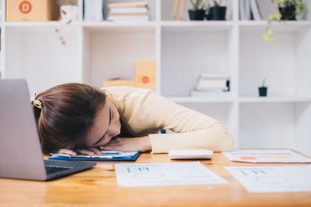Asian business woman sleeping on table after hard work to audit transactions account budget of company. Accountant and Anti Bribery concept.の写真素材