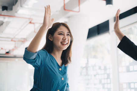 Asian businesswoman and her partners give each other high fives as they celebrate a successful team...