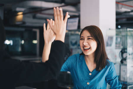 Asian businesswoman and her partners give each other high fives as they celebrate a successful team building project.の写真素材