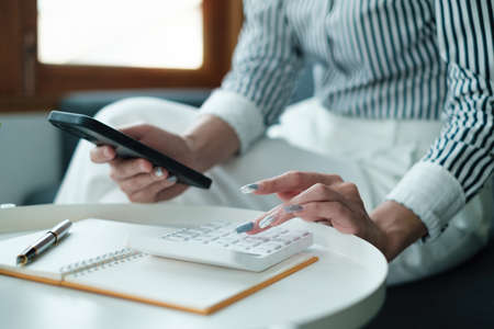 Business woman hand holding pen looking at bank savings account application on cell phone. account...