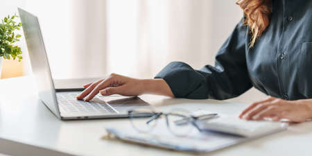 Close up Business woman hand using calculator to calculate on laptop the companys financial results...