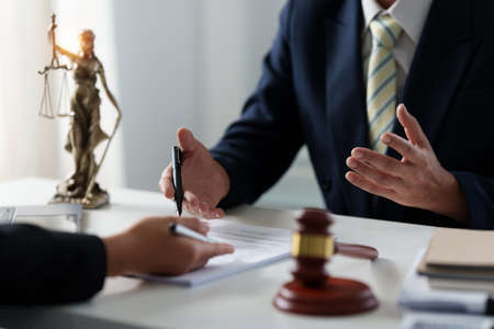 Business woman and lawyers discussing contract papers with brass scale on wooden desk in office....