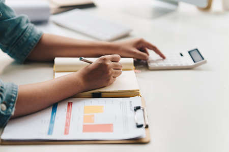 Asian Business Woman or Accountant do math and analyze with calculator and paperwork on desk,...