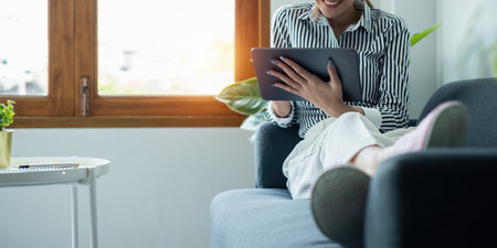 Woman enjoy with content streaming movies or social media application on digital tablet sitting near sofa at home.の写真素材