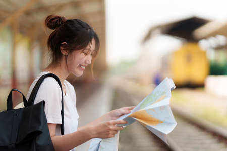 Young traveler woman looking on maps planning trip at train station. Summer and travel lifestyle concept.の写真素材