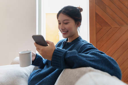 Portrait of Young Asian woman chatting with her friend and checking social media by smartphone...