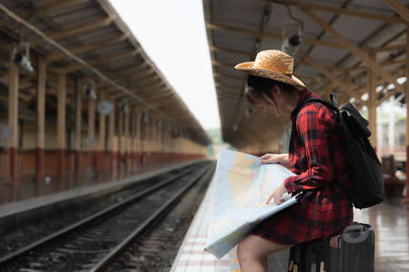 Pretty Young traveler woman looking on maps planning trip at train station. Summer and travel lifestyle concept.の写真素材