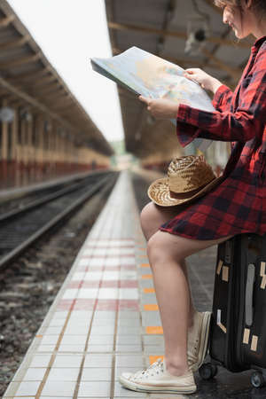 Pretty Young traveler woman looking on maps planning trip at train station. Summer and travel lifestyle concept.の写真素材
