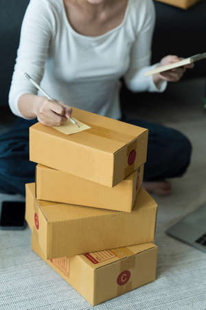 Asian woman, e-commerce employee freelance with parcel box for deliver to customer. Online marketing packing box delivery concept.の写真素材