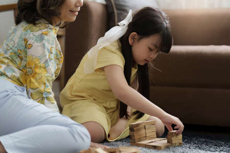 Girl playing wooden jenga constructor with grandmother at home. Leisure activities for children at...