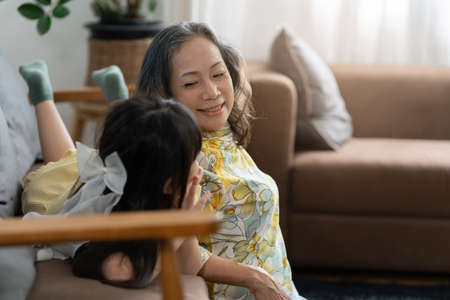 Happy moments of Asian grandmother with her granddaughter talking together in living room at home.
