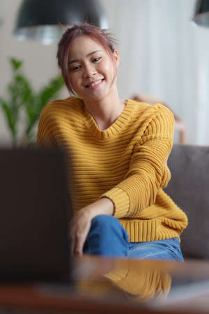 Portrait of happy asian beautiful girl making video calling with laptop and waving on phone screen...