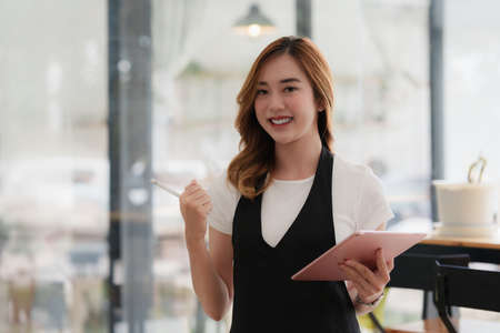 Beautiful Asian women Barista smiling and using tablet at her cafe