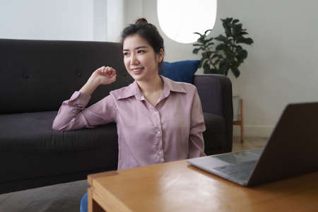 Asian woman using laptop and sitting on sofa at home office
