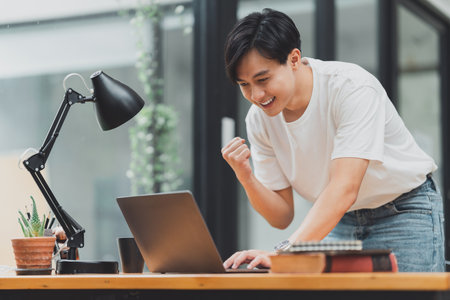 Happy Asian man using laptop computer while have a good news working at officeの写真素材