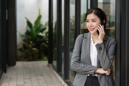 Young asian business woman smiling and talking on mobile phone, standing outside building