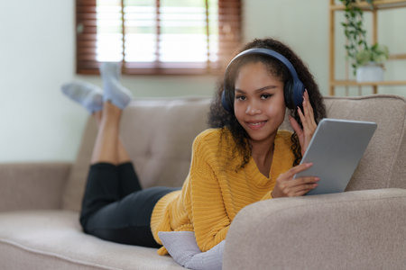 Attractive smiling young woman using tablet and listen music on sofa at home. lifestyle conceptの写真素材
