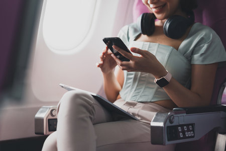 Young asian woman using smartphone connected to wifi internet during flight on board. Travel conceptの写真素材