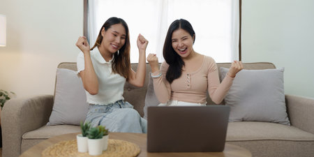 Two asian women having nice lively conversation in living room on sofa in cozy interiorの写真素材